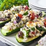 close up view of Greek Chicken Stuffed Zucchini Boats with plates in the background
