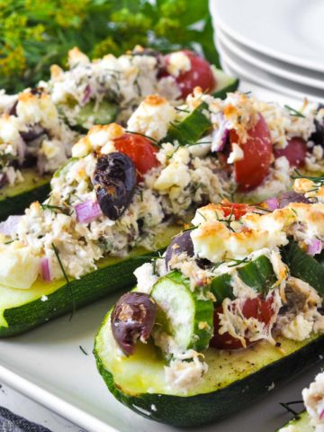 close up view of Greek Chicken Stuffed Zucchini Boats with plates in the background