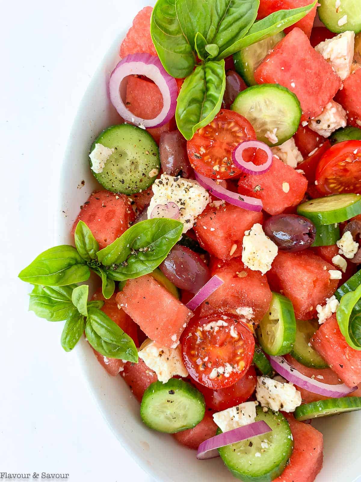 Greek Watermelon Basil Salad in a white oval bowl with basil leaves