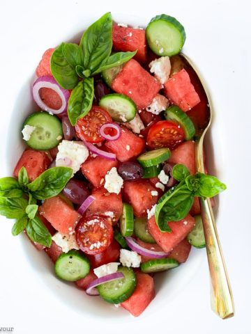 Greek Watermelon Basil Salad in an oval bowl with a gold spoon