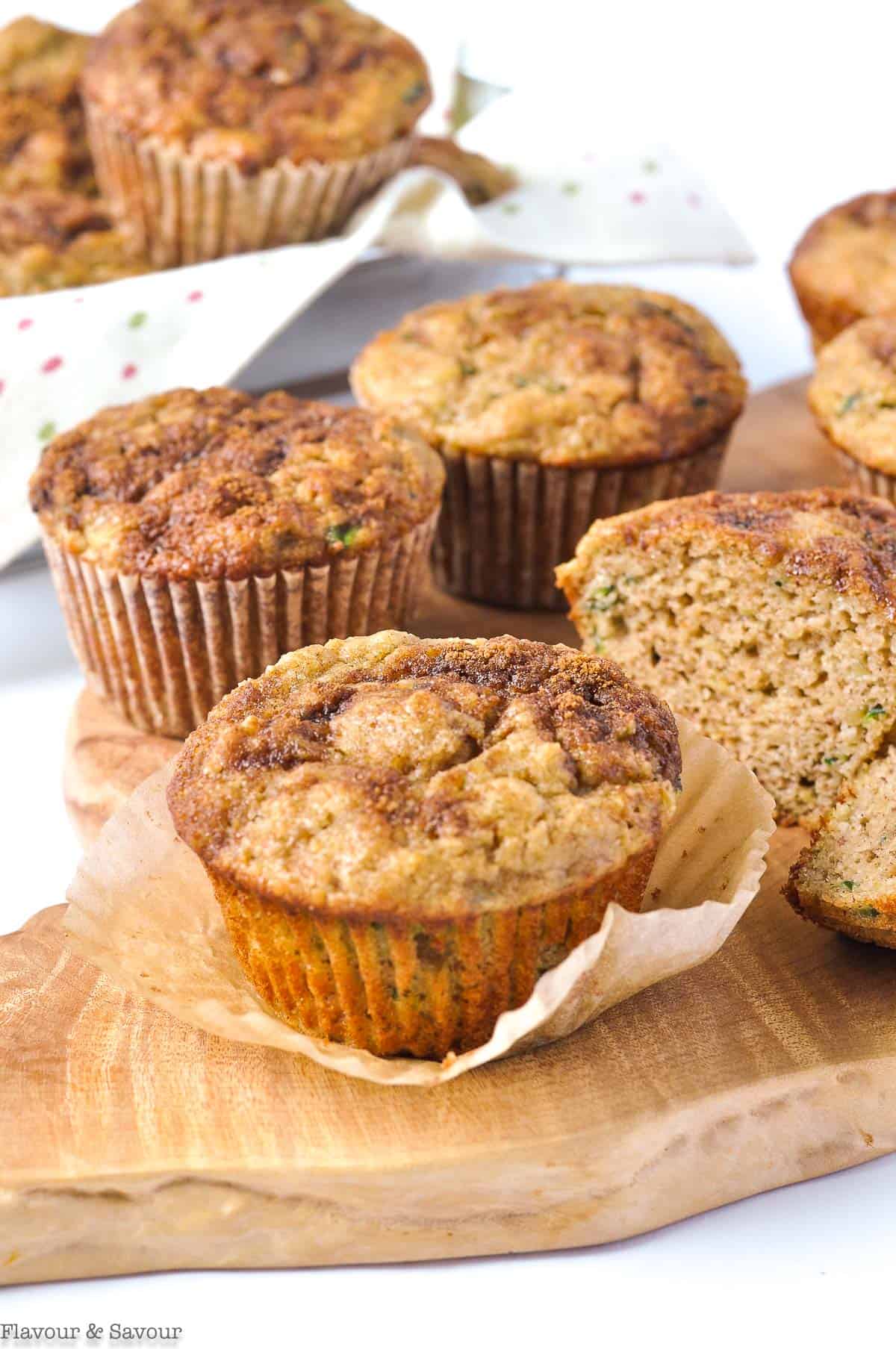 Zucchini Banana Muffins on a board with a basket of muffins in the background.