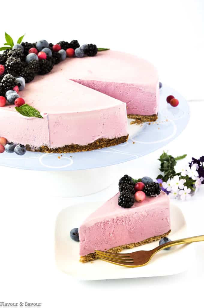 Blackberry Ice Cream Cheesecakeon a pedestal stand with a slice on a plate with a fork