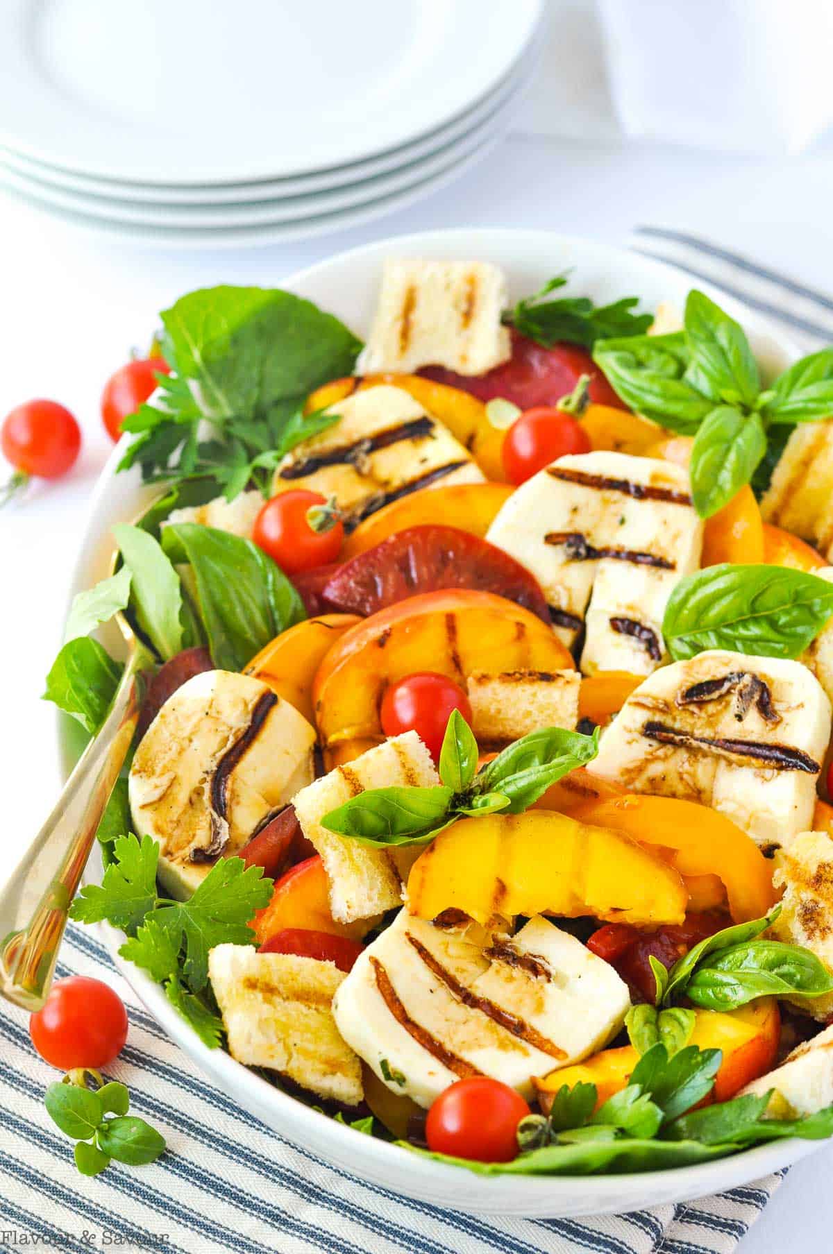 Grilled Halloumi Peach and Tomato Salad in a serving bowl with a stack of white plates.