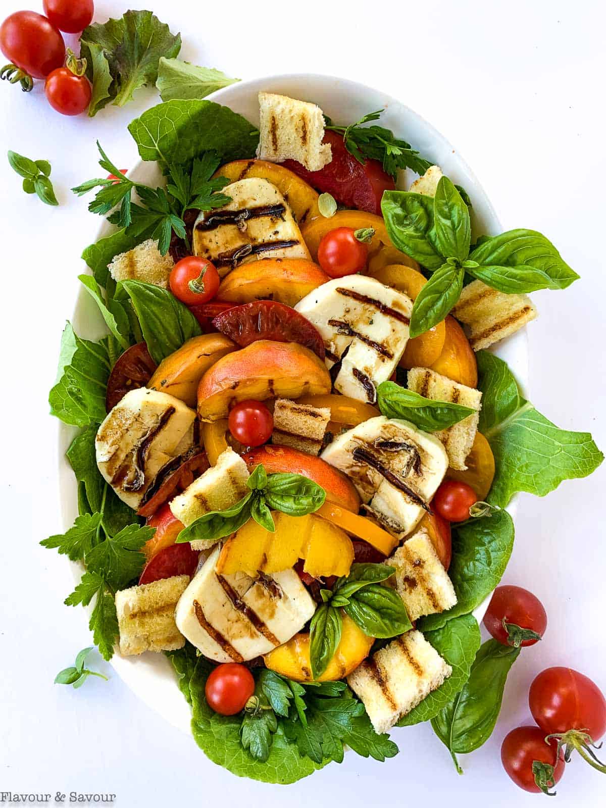 Overhead view of Grilled Halloumi Peach and Tomato Salad garnished with basil leaves.