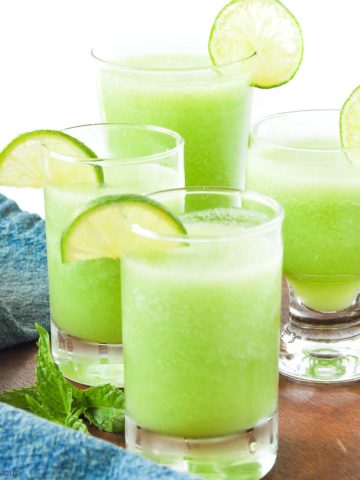 Four glasses of honeydew lime mocktail with lime slices for garnish