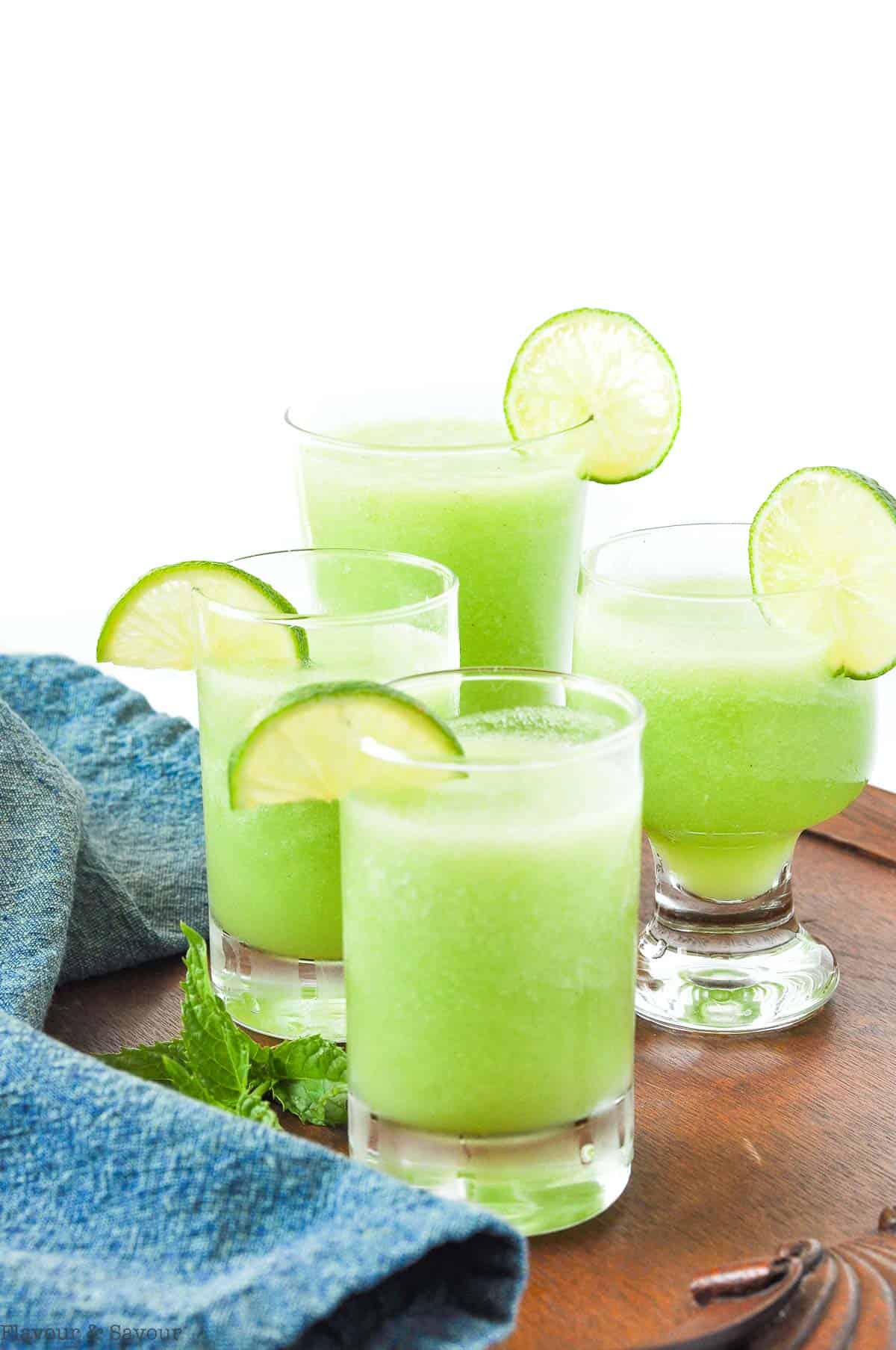 Four glasses of Honeydew Lime mocktail garnished with lime slices