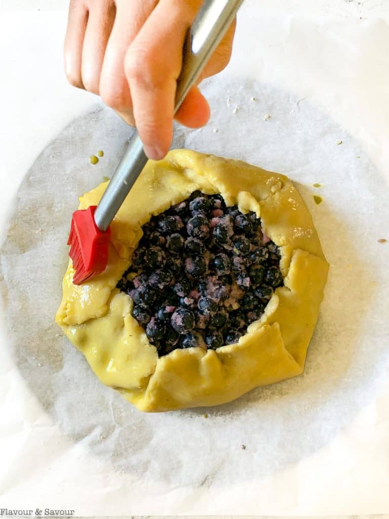 brushing egg wash on galette pastry for blueberry lemon galette