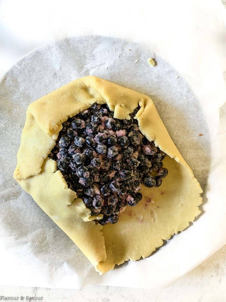 Folding galette pastry around blueberry filling to make blueberry lemon galette