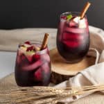 Two glasses of Cranberry Apple Cider Sangria garnished with fruit and a cinnamon stick