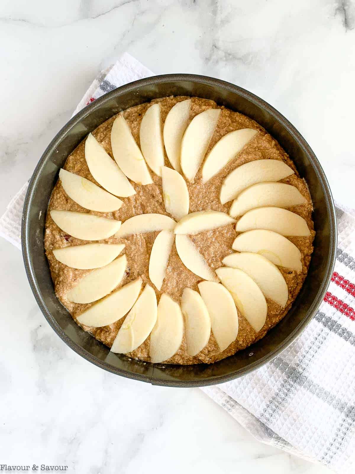 Apple slices arranged in a concentric pattern on top of applesauce cake batter in a springform pan.