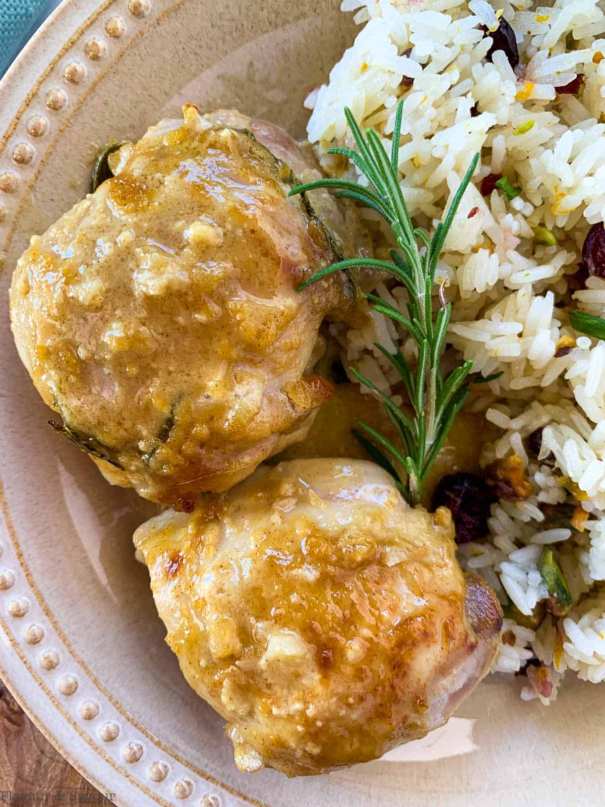 Close up view of two Maple Dijon Chicken Thighs on a plate with rosemary sprig and rice