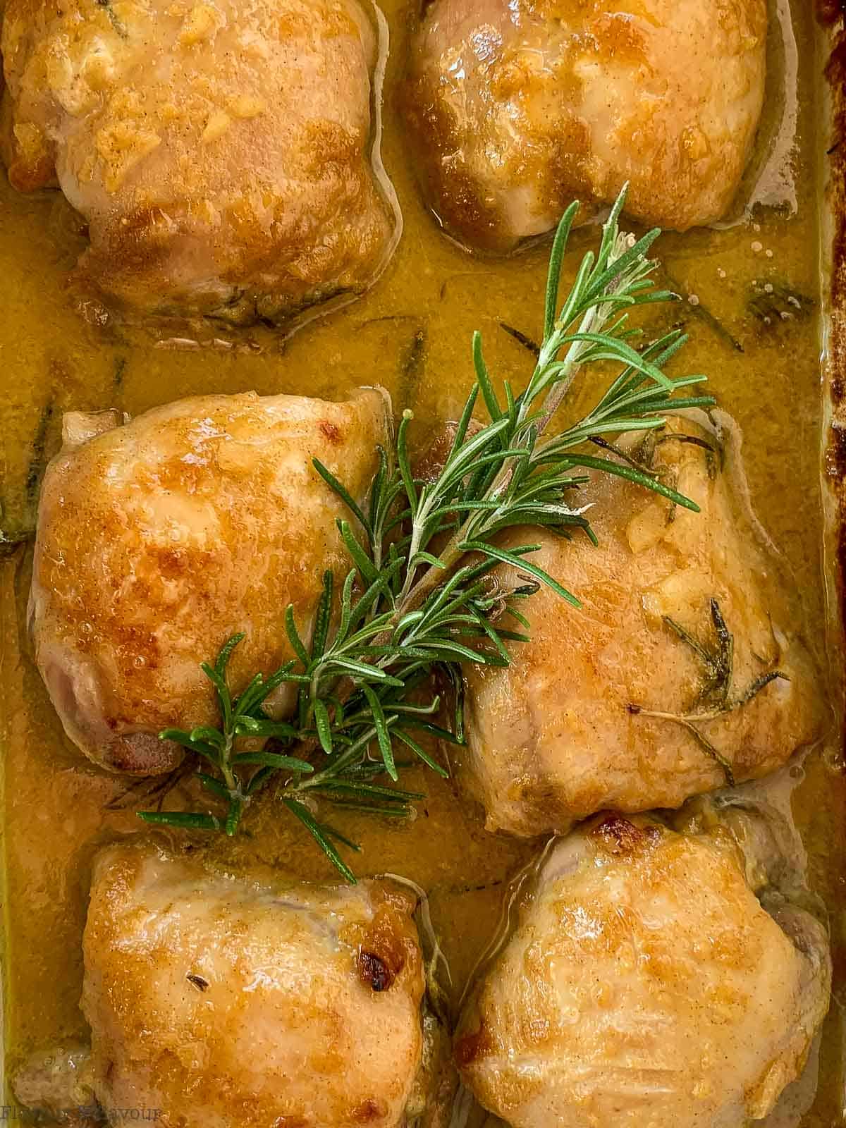 Maple Dijon Chicken thighs in a baking dish with a sprig of fresh rosemary.