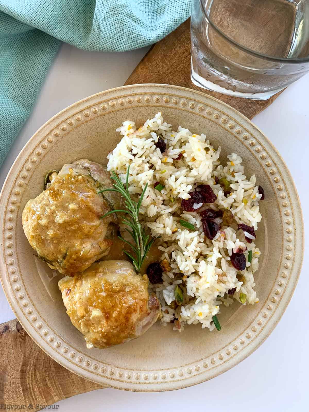 Cranberry Pistachio Jasmine Rice on a plate with chicken thighs and a sprig of rosemary.