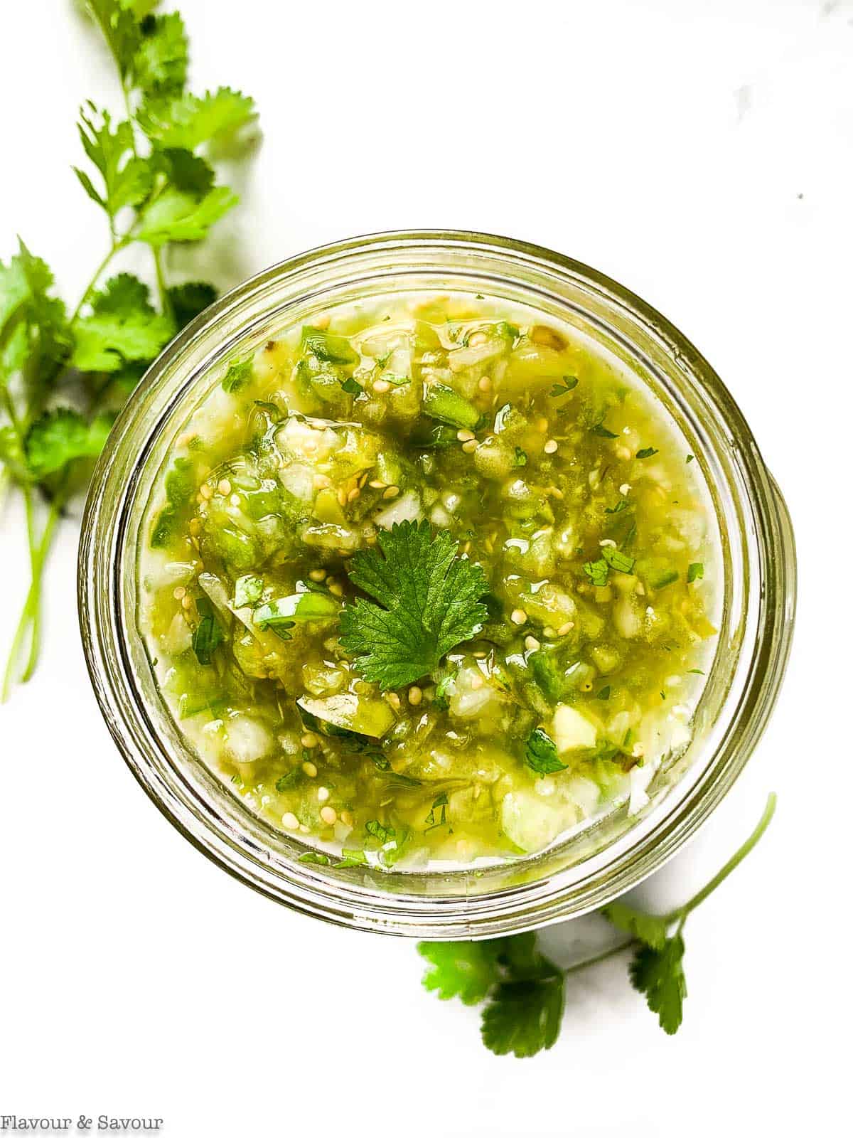 Roasted Tomatillo Salsa Verde in a Mason Jar with cilantro sprigs beside.