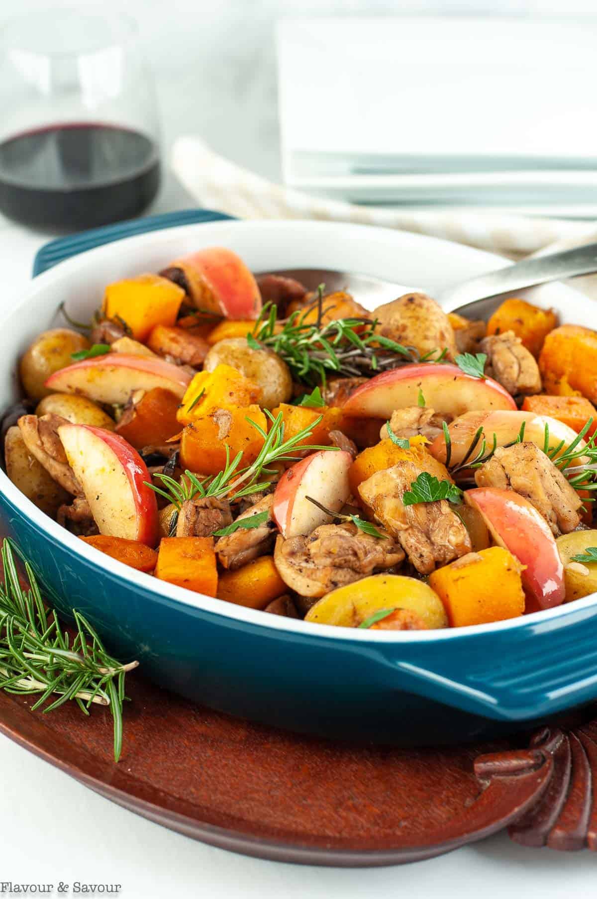 Side view of Harvest Chicken in serving dish with a spoon and a glass of red wine in the background