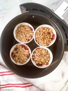 Four ramekins with cherry crisp in an air fryer basket