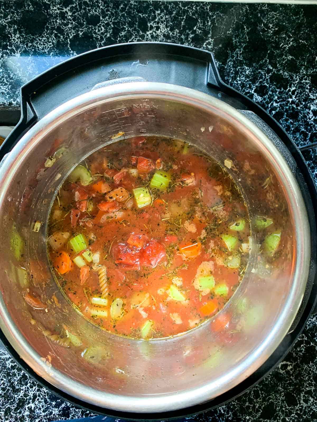 Preparing Minestrone Soup step 2, adding broth, herbs, tomatoes and pasta to the pot.