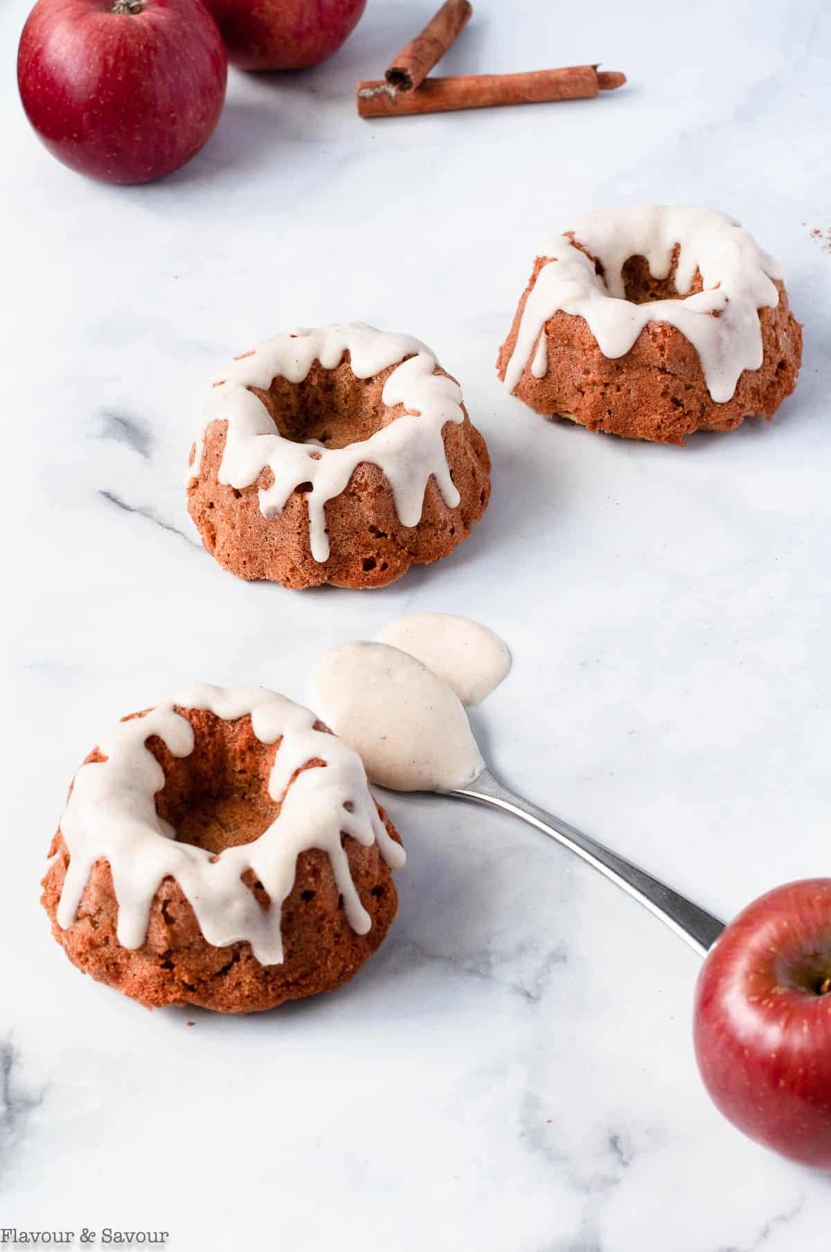 Three Mini Apple Bundt Cakes with a spoonful of Cinnamon Cream Cheese Glaze