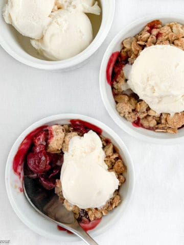 Two ramekins with Cherry Almond Crisp with a dish of ice cream