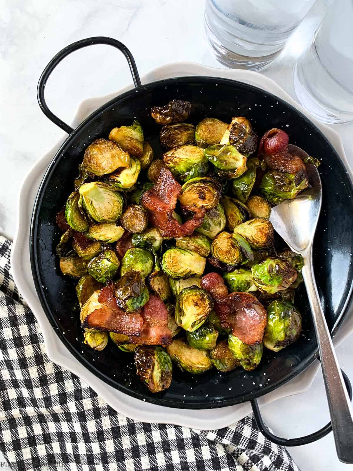 Air Fryer Brussels Sprouts with Bacon in a black serving dish with a black and white checkered cloth beside it.