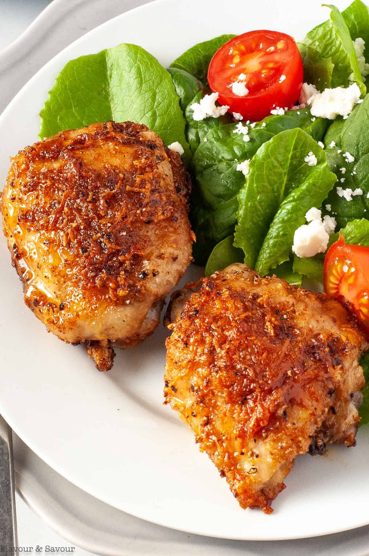 Two garlic parmesan chicken thighs on a plate with salad