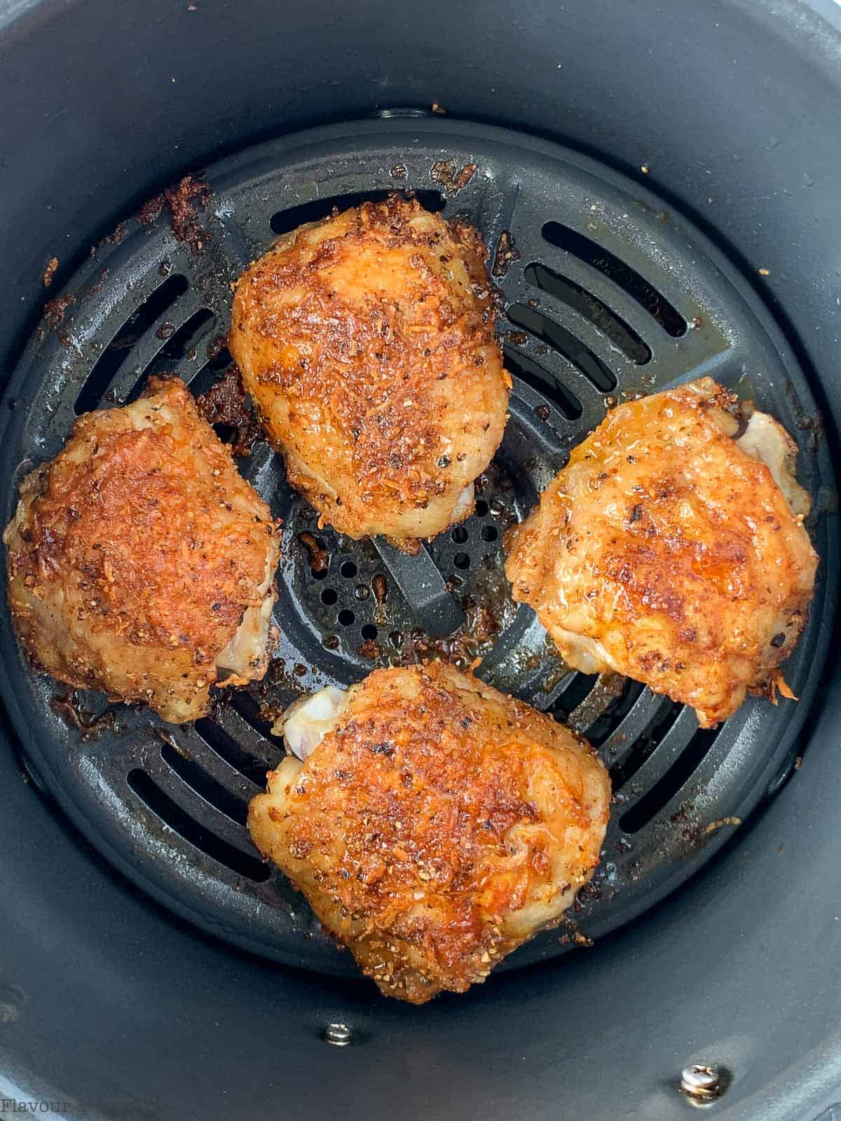 Four cooked chicken thighs in air fryer basket