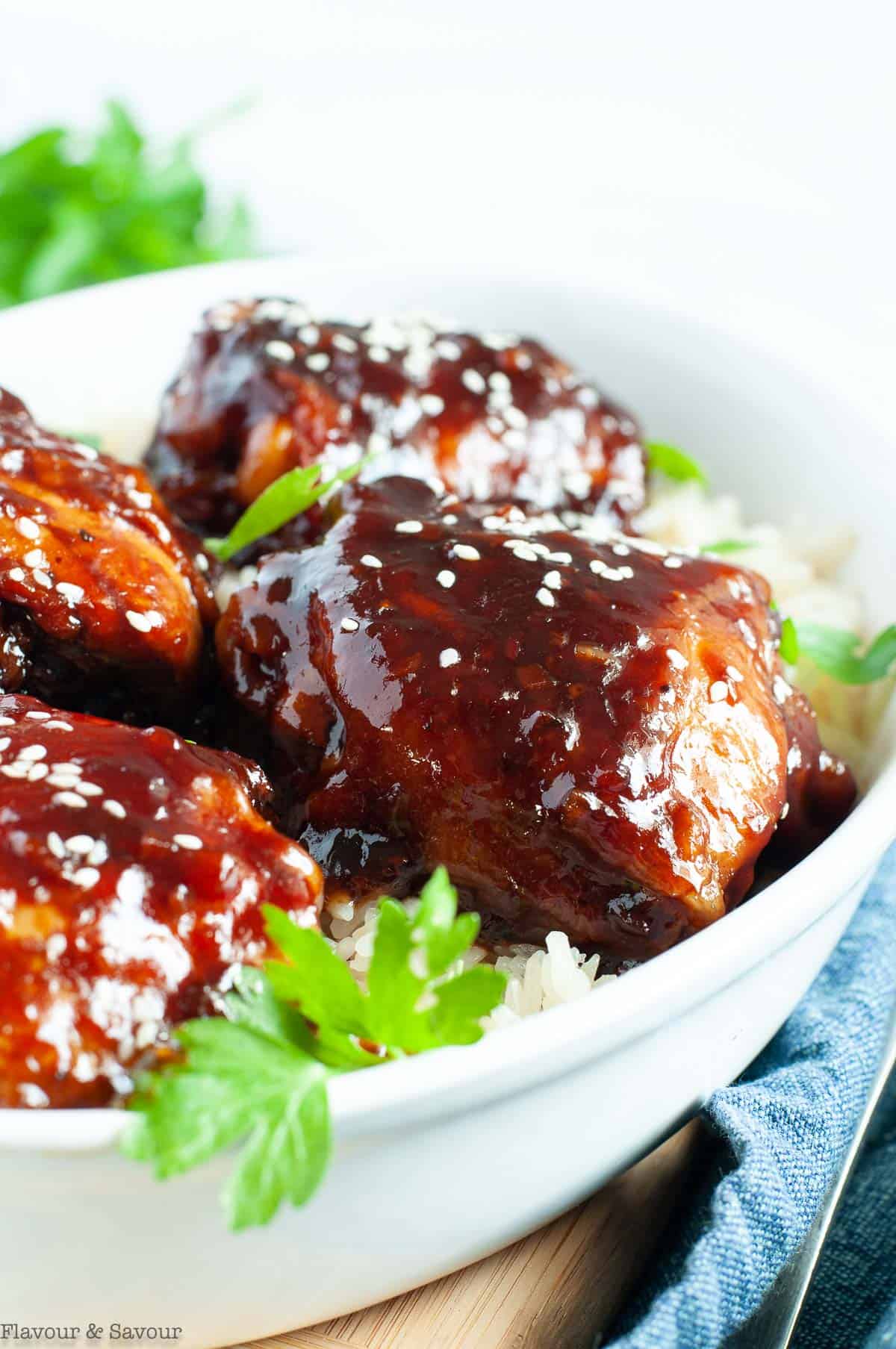 Close up view of Sticky Chicken Thighs in a white bowl with cilantro leaves