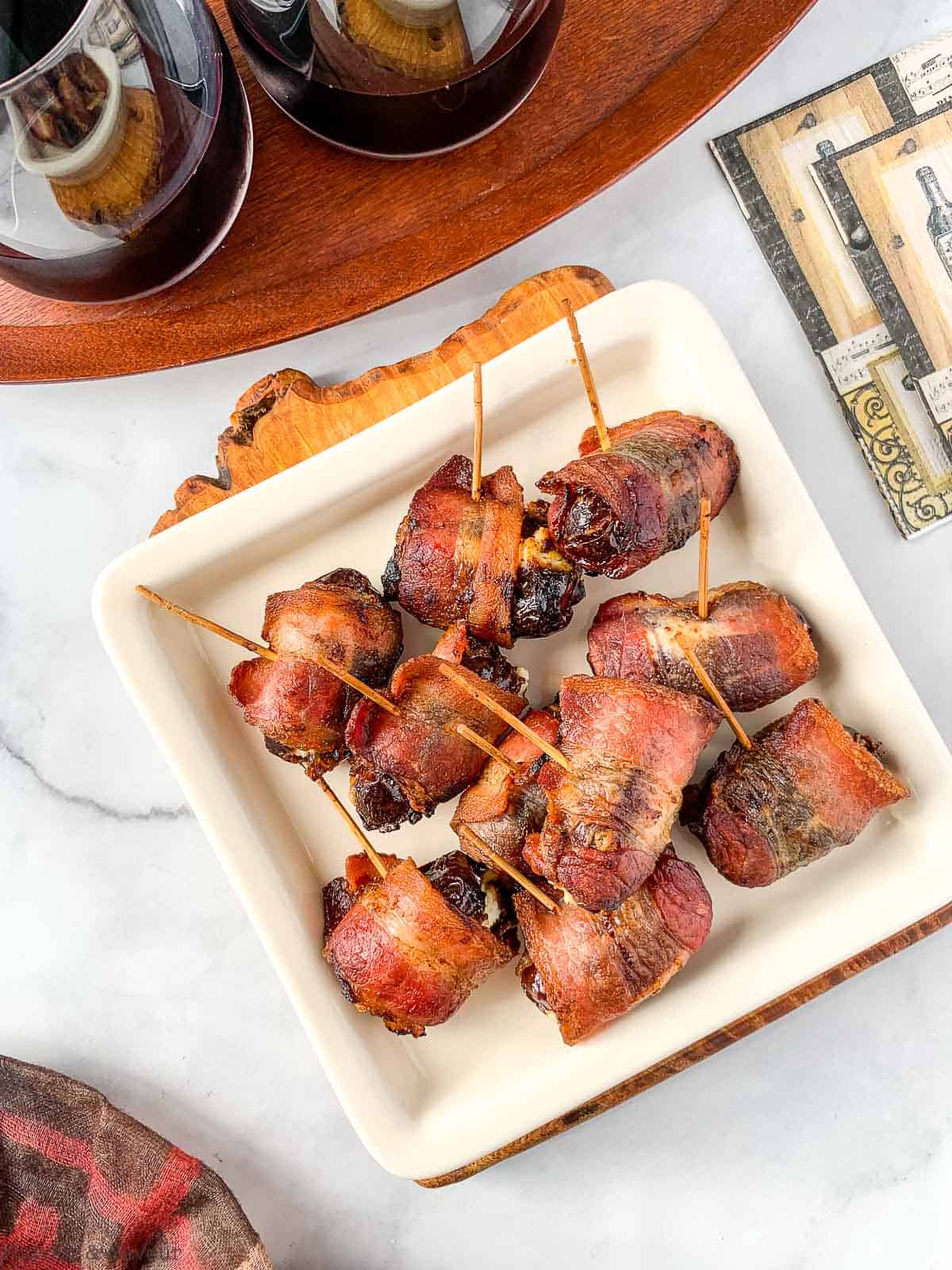 A square plate of bacon wrapped dates with two glasses of wine
