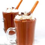 Two mugs of Mexican Hot Chocolate with whipped cream and cinnamon sticks.