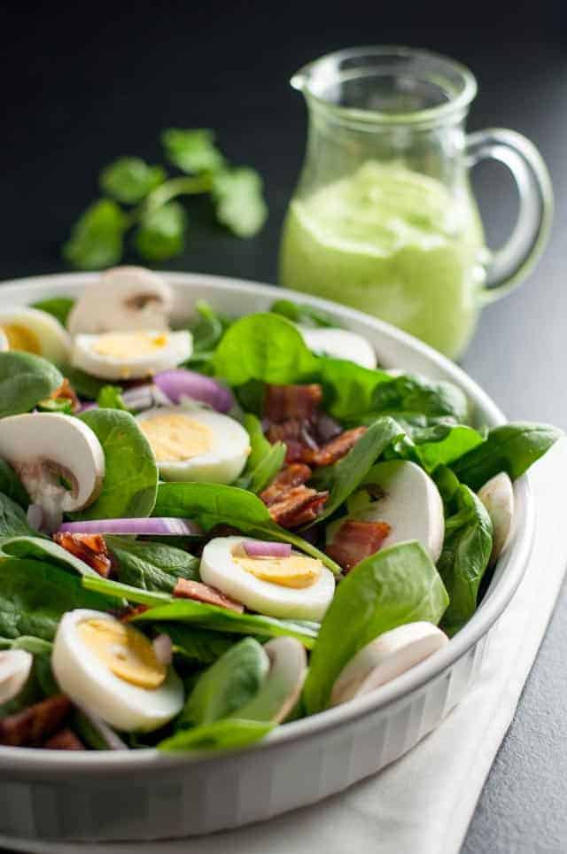 A shallow bowl of spinach salad with eggs and bacon