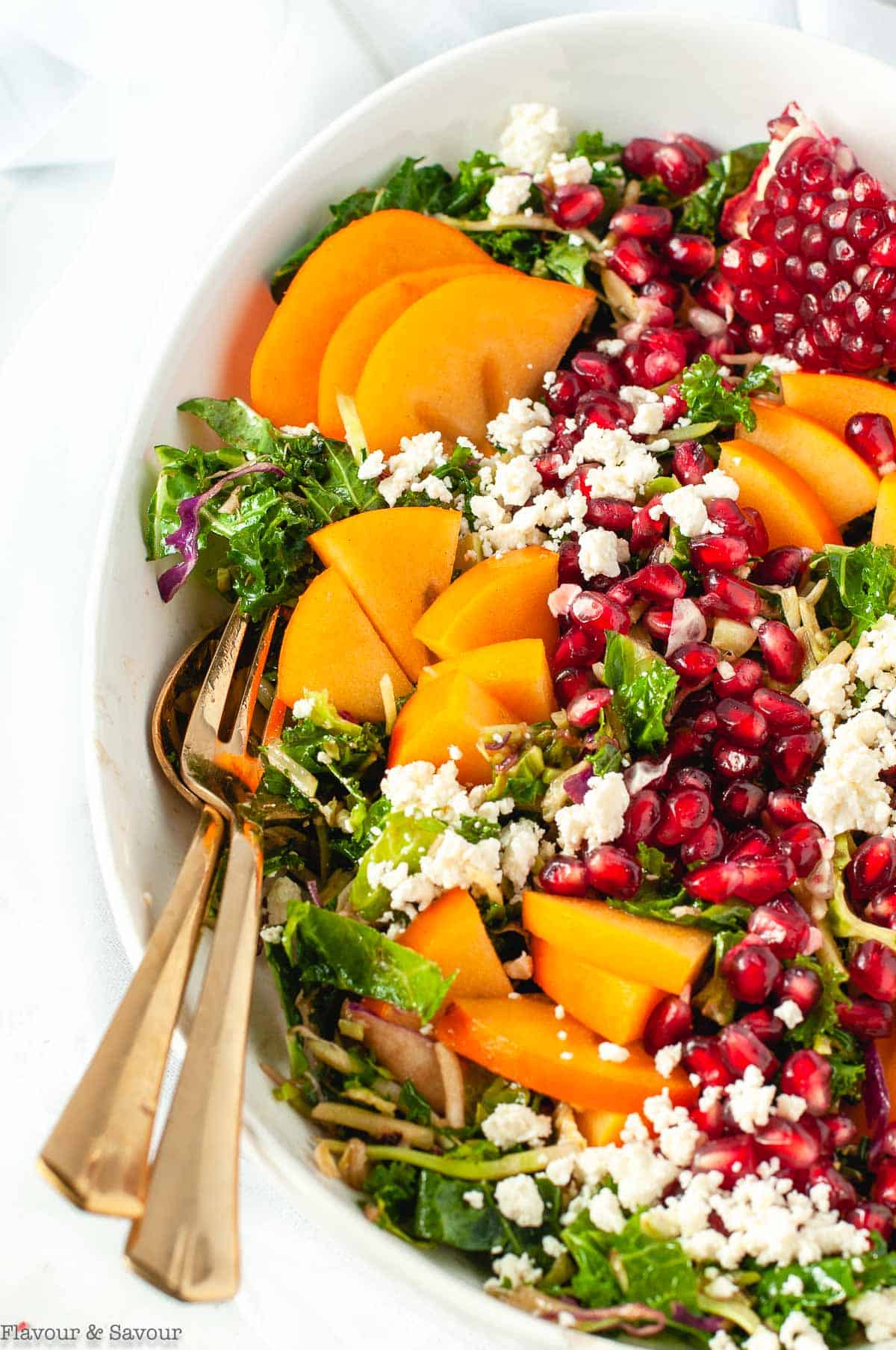 Winter Pomegranate Persimmon Kale Salad in a serving bowl with salad servers.