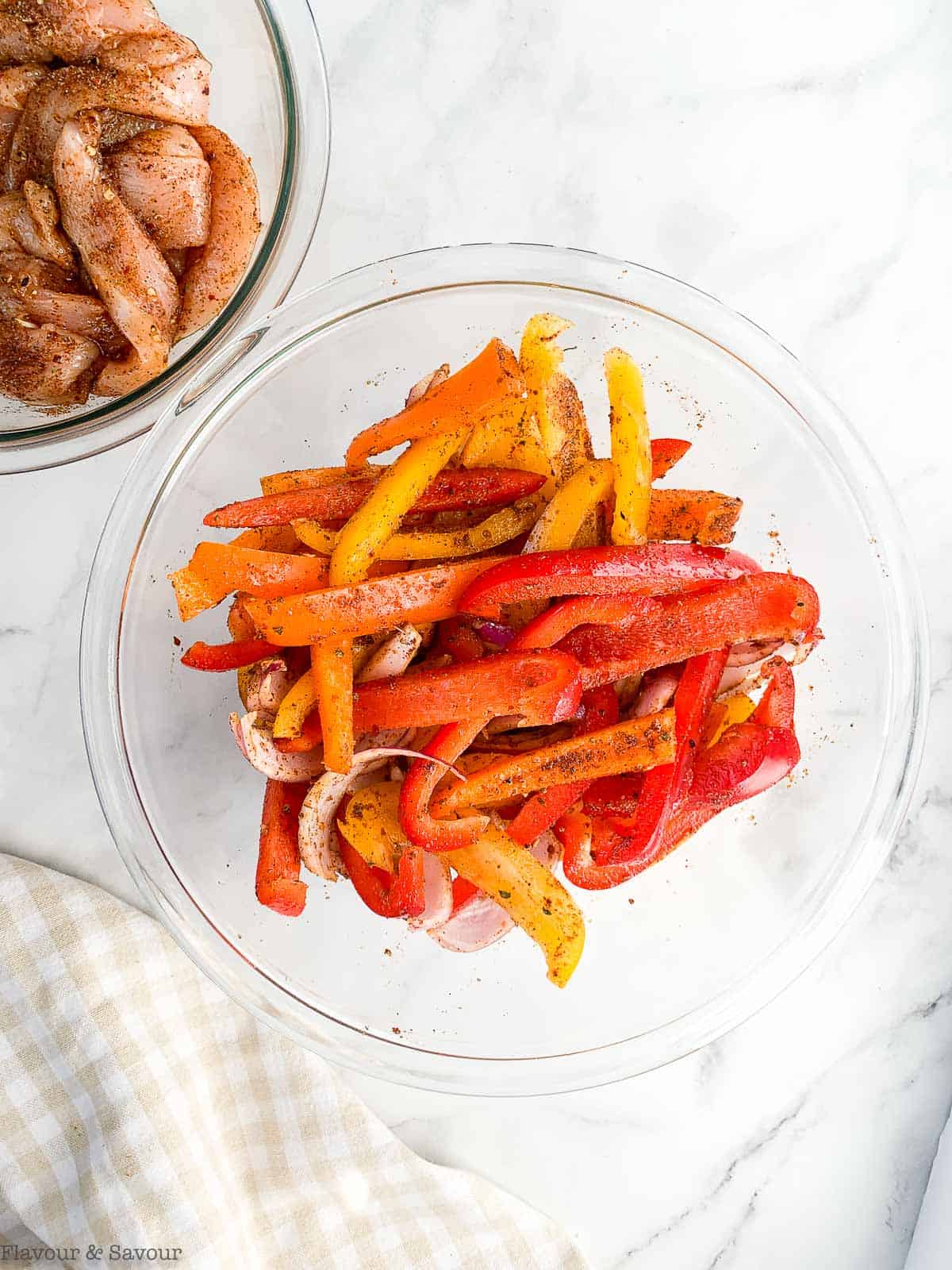 A bowl of sliced bell peppers and one of sliced chicken tossed with oil and fajita seasoning