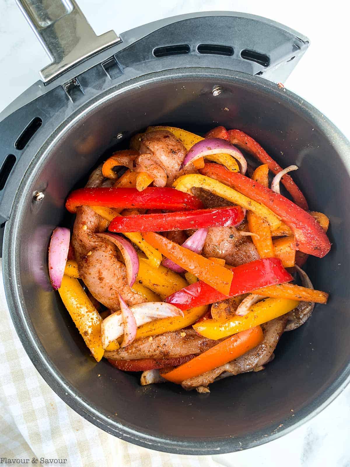 Sliced peppers and chicken in an air fryer basket