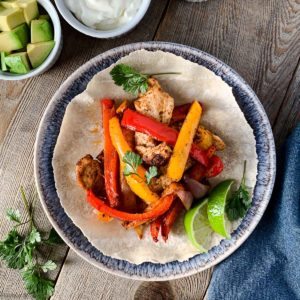 Overhead image of Chicken Fajitas on a blue plate with avocado and lime