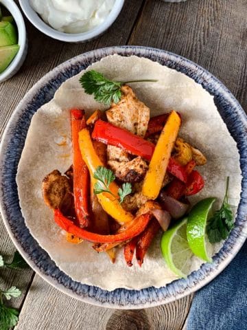 Overhead image of Chicken Fajitas on a blue plate with avocado and lime