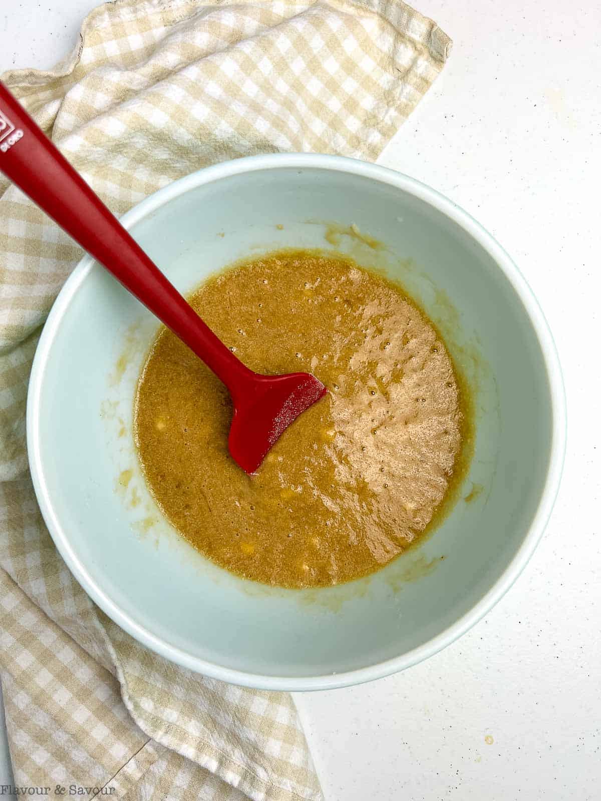 Wet ingredients for banana coffee cake in a bowl with a spatula.