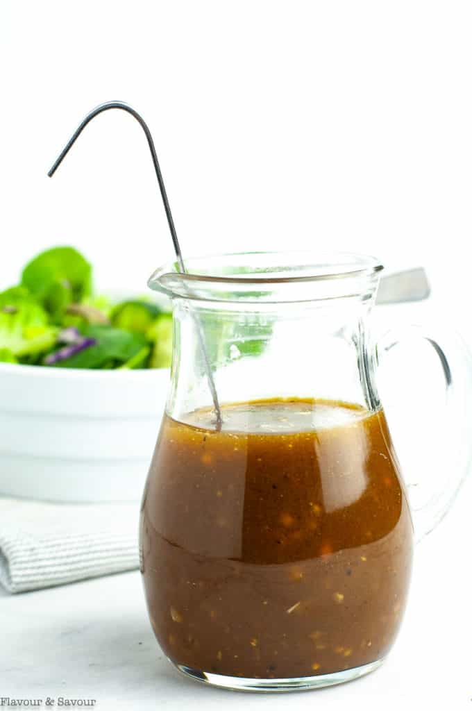 A small pitcher of Maple Balsamic Dressing with a salad