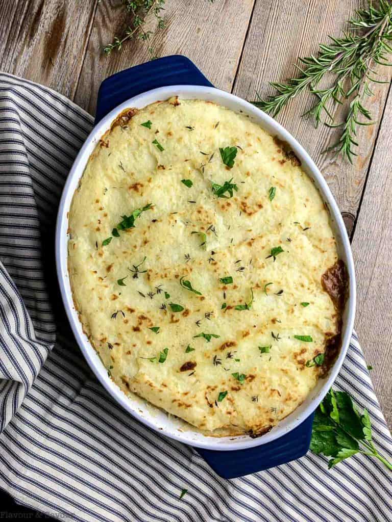 Shepherd's Pie baked on a striped blue cloth with fresh herbs 