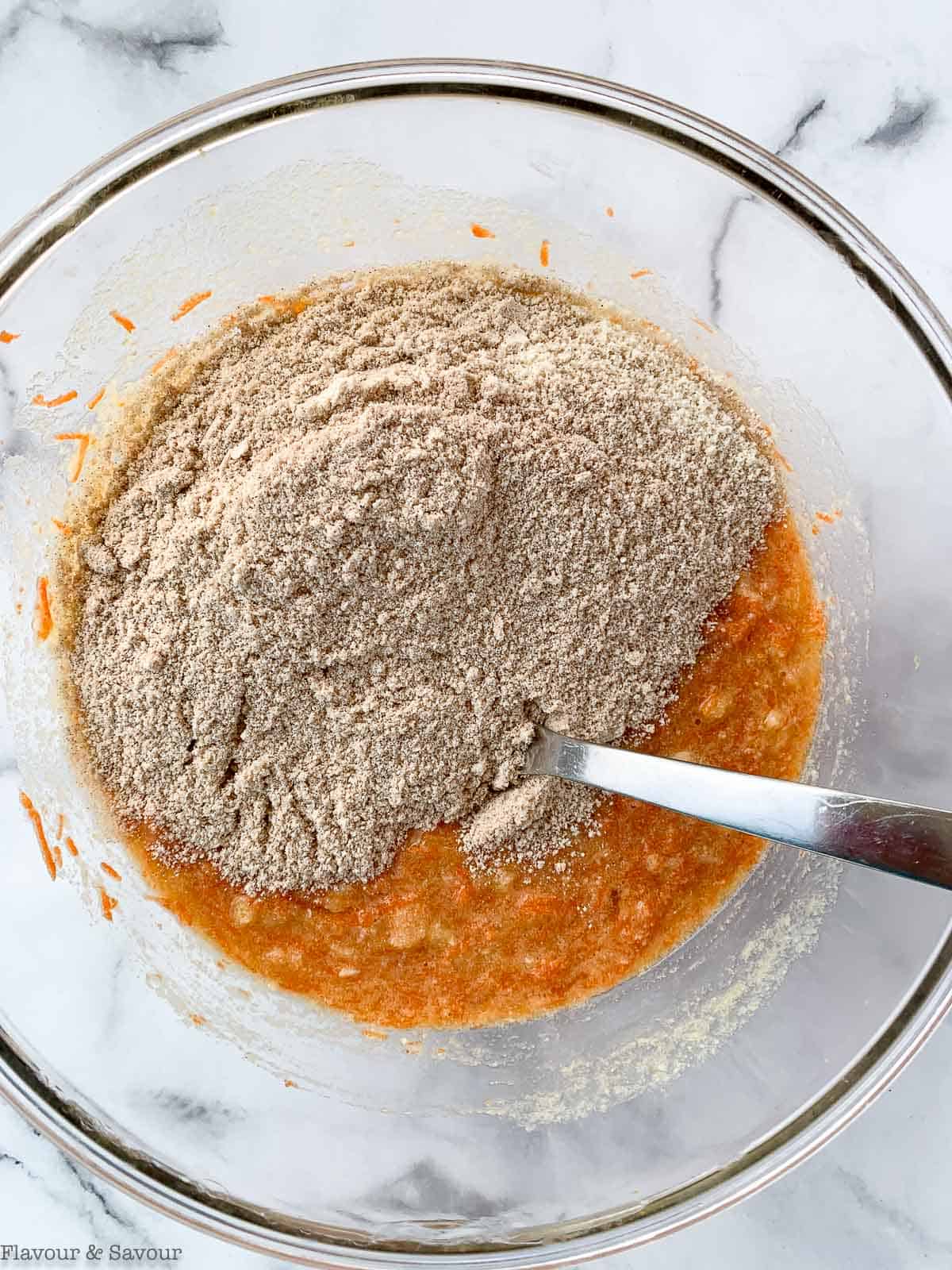 Adding dry ingredients to wet ingredients to make mini carrot cake cupcakes.