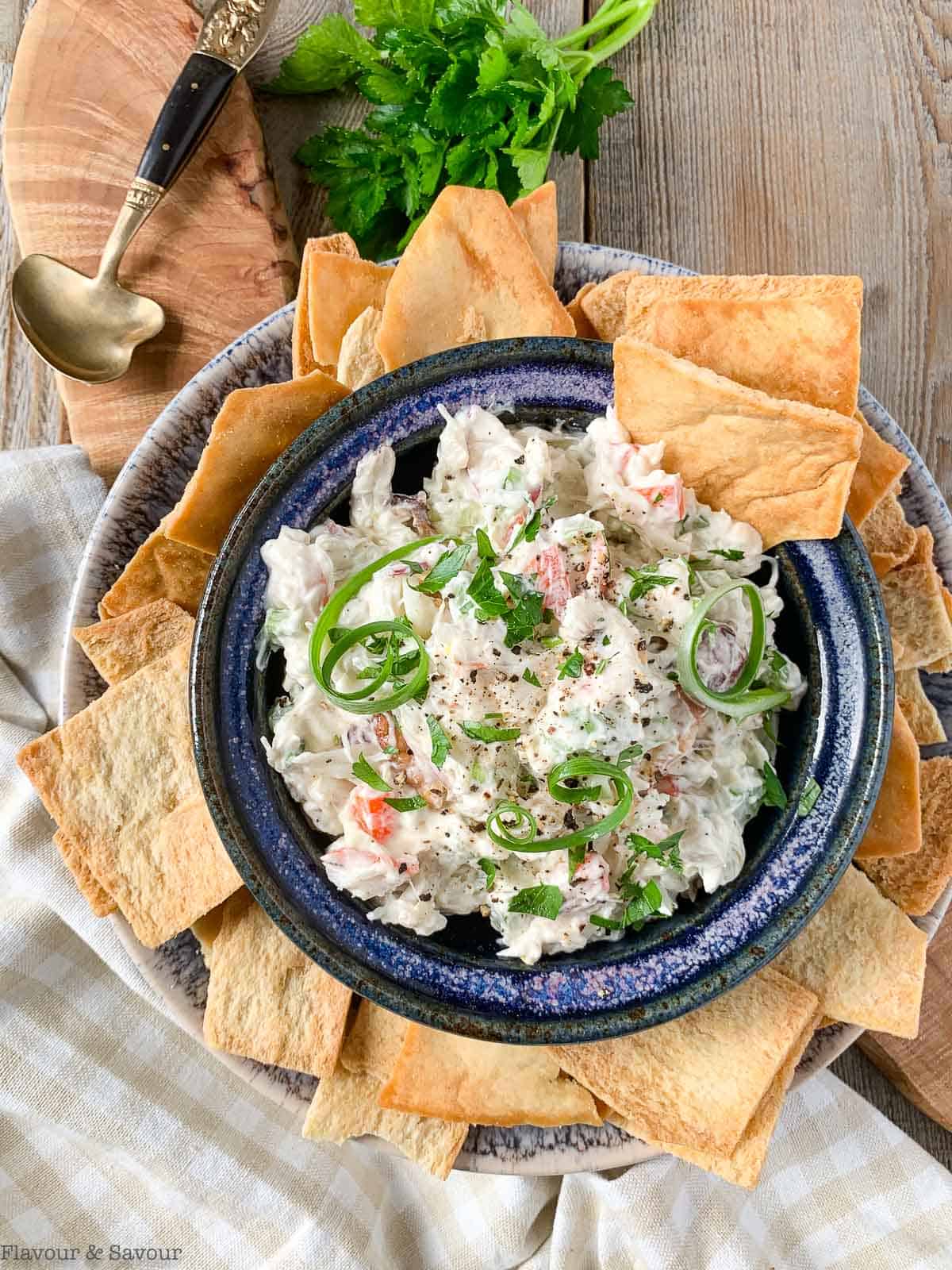 Overhead view of a bowl of cold crab dip surrounded by pita chips.