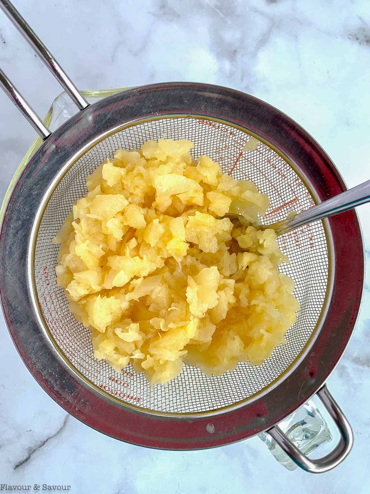 Draining crushed canned pineapple in a sieve.