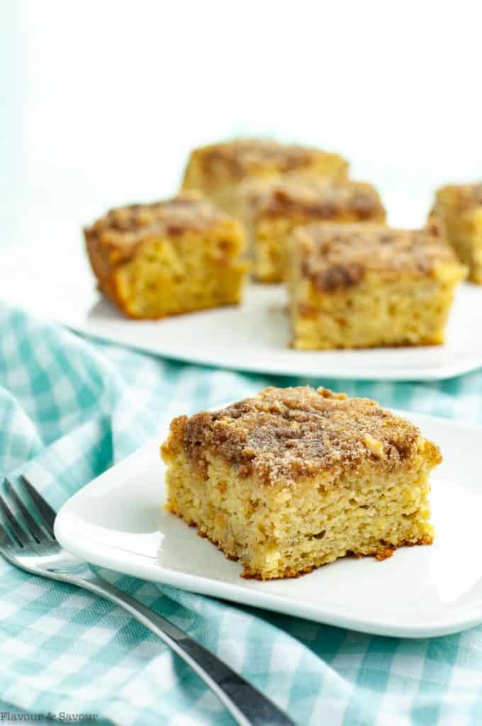 A square of grain-free banana coffee cake with a plate of cake in the background