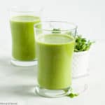 Two glasses of Pineapple Orange Green Smoothie with a dish of microgreens