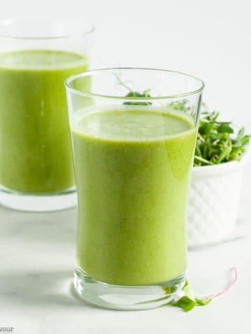 Two glasses of Pineapple Orange Green Smoothie with a dish of microgreens