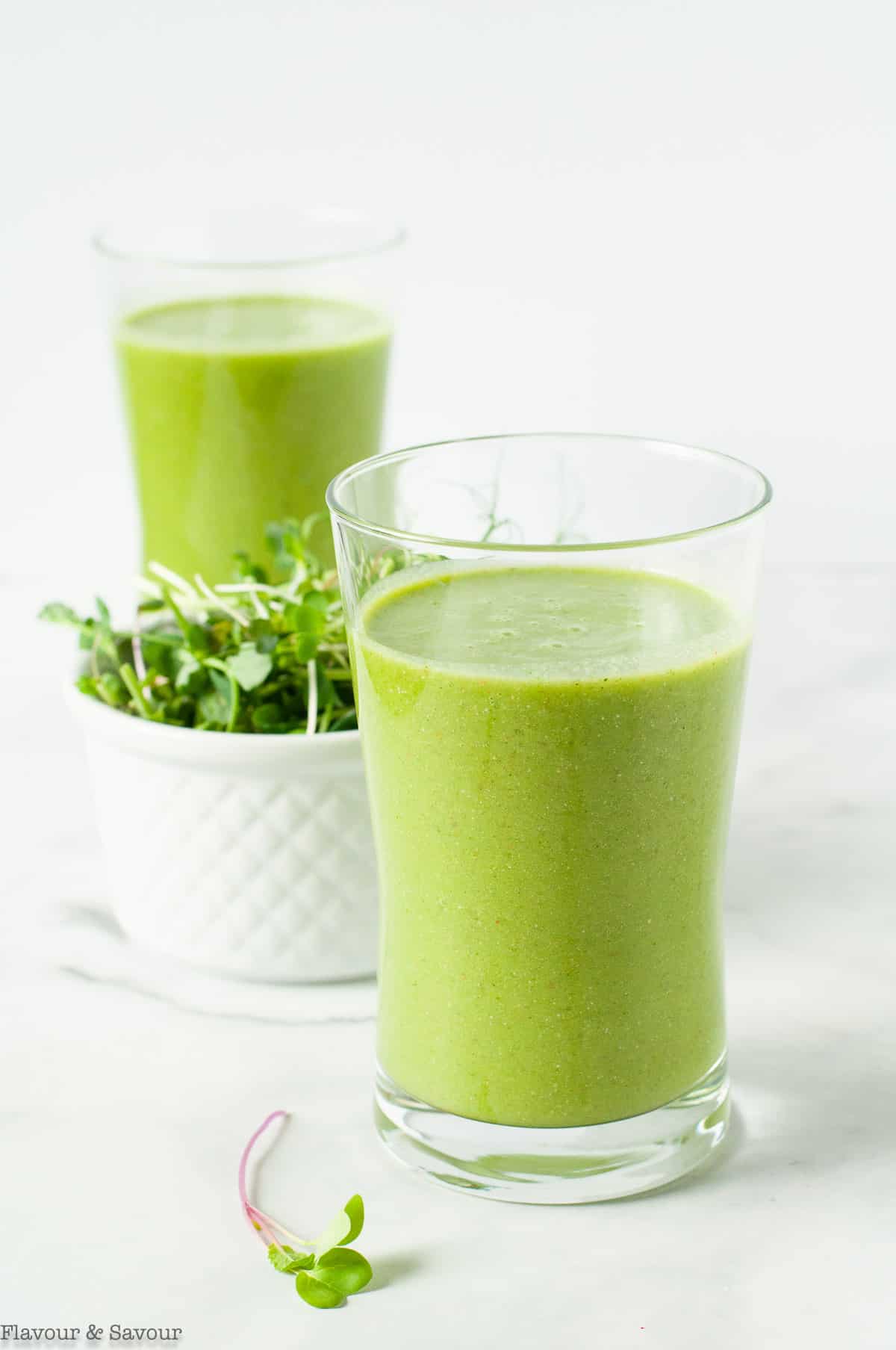 Two glasses of pineapple orange green smoothie with a small bowl of microgreens, an idea for a healthy smoothie recipe
