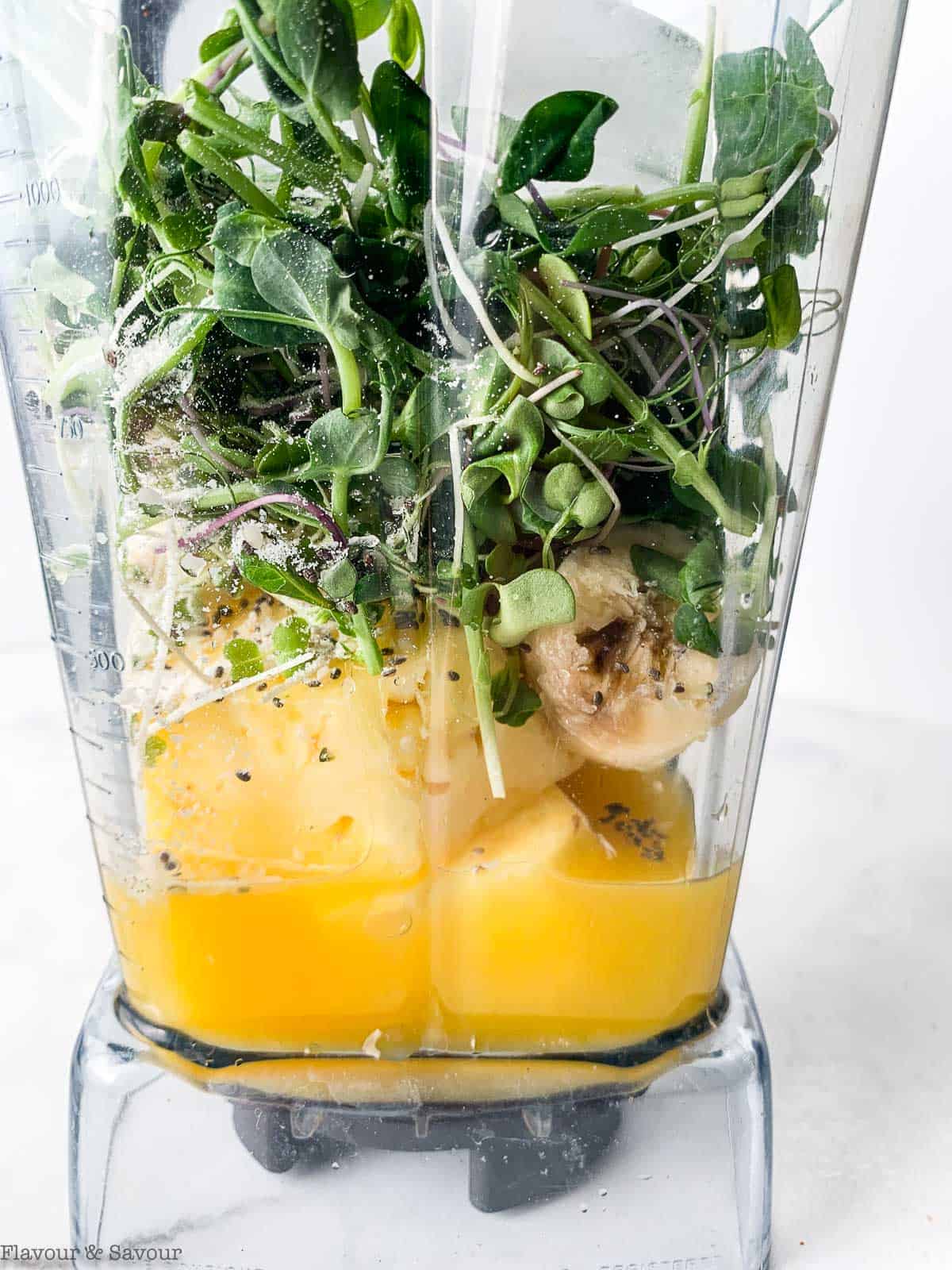 A blender container with ingredients for a green smoothie