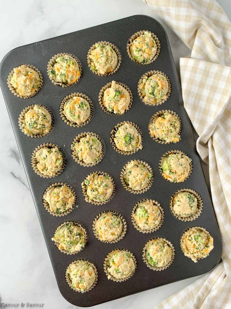 Mini muffin tin filled with broccoli cheddar muffin batter.