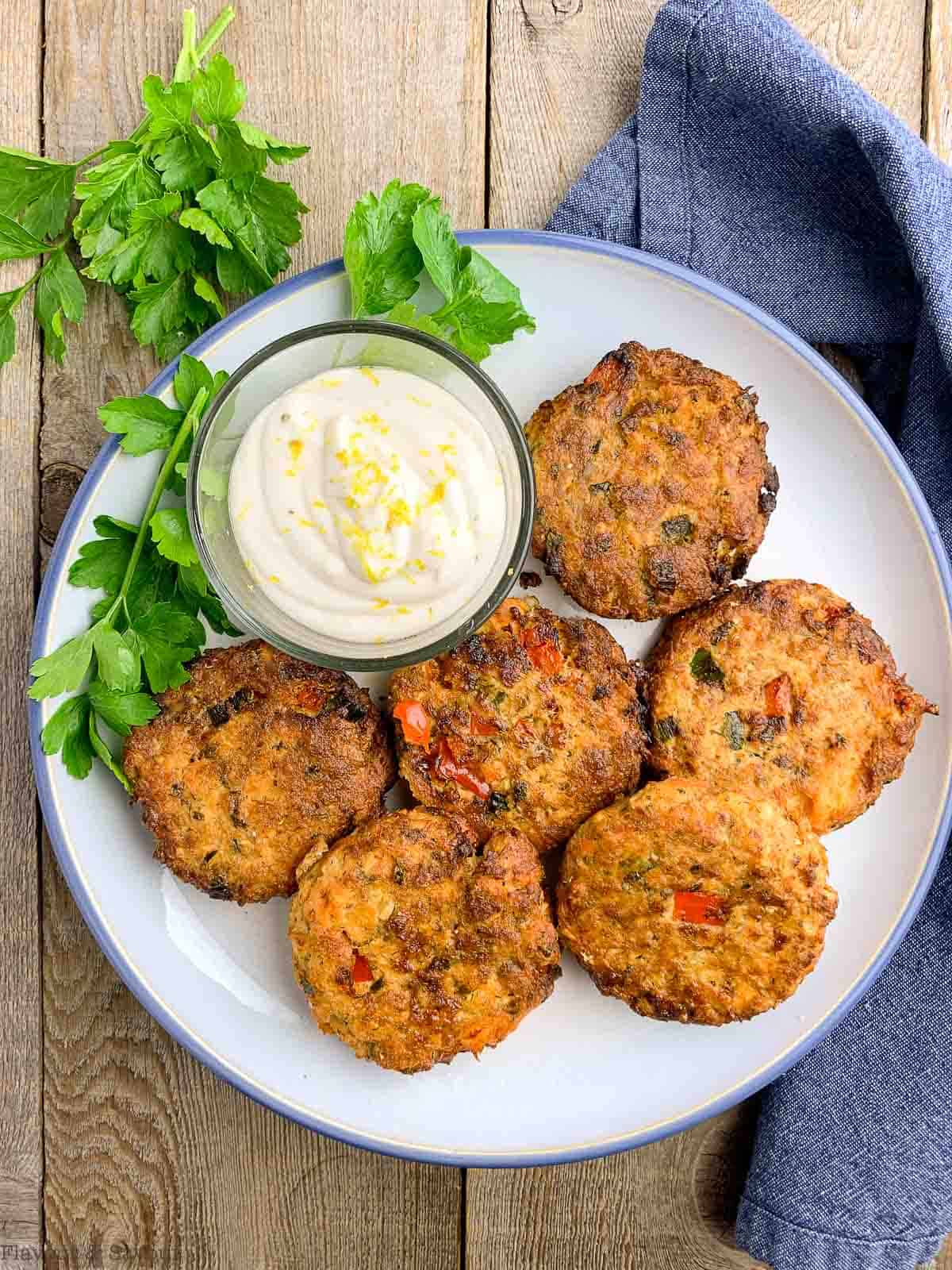 Overhead view of 6 salmon cakes on a plate with lemon aioli dip