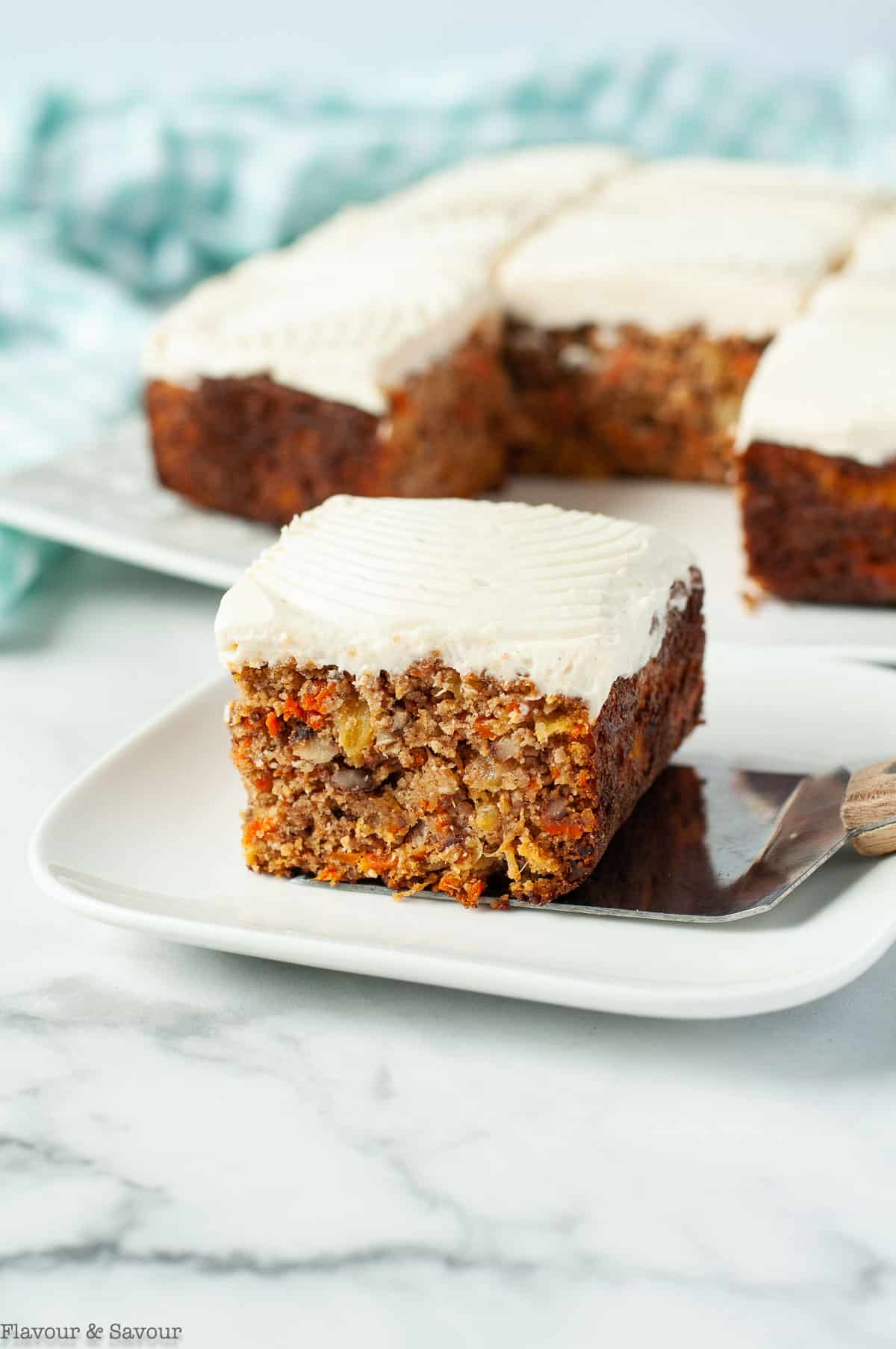 A square of carrot cake with the remaining cake in the background