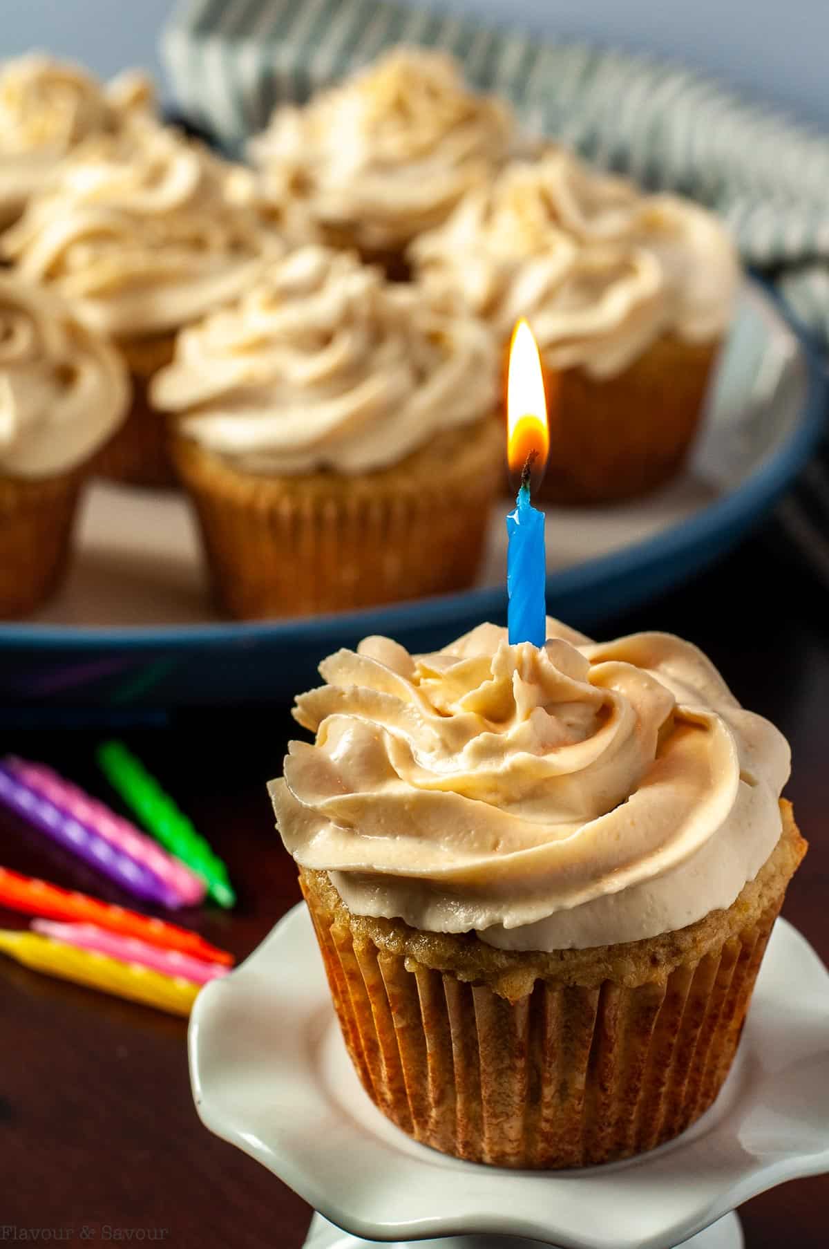 A frosted banana cupcake with a lit birthday candle